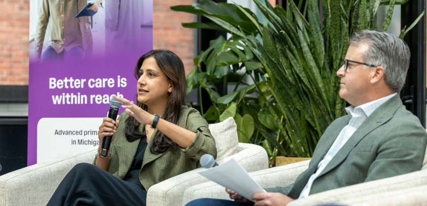 Dr. Avani Sheth, a panelist in a green jacket, speaks at a Marathon Health panel in Detroit next to a banner that reads "Better care is within reach. Advanced primary care in Michigan."