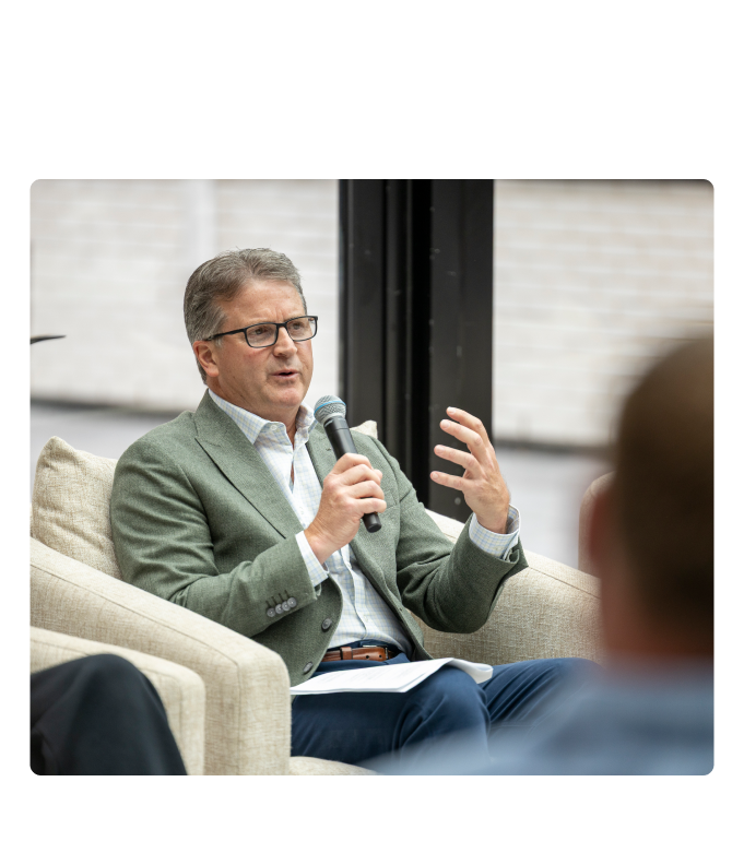 Chris Pricco, chief executive officer of Marathon Health, wears a sage-green blazer and glasses. He gestures while speaking into a microphone at a Marathon Health panel on advanced primary care and behavioral health in Detroit.