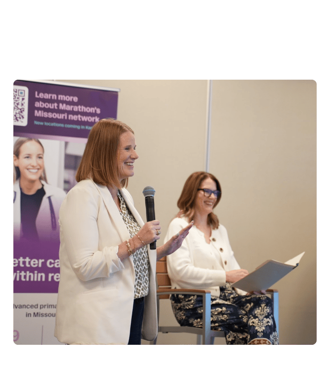 A speaker addresses a Marathon Health panel in Kansas City as Kansas City Business Journal Publisher Stacie Prosser listens.