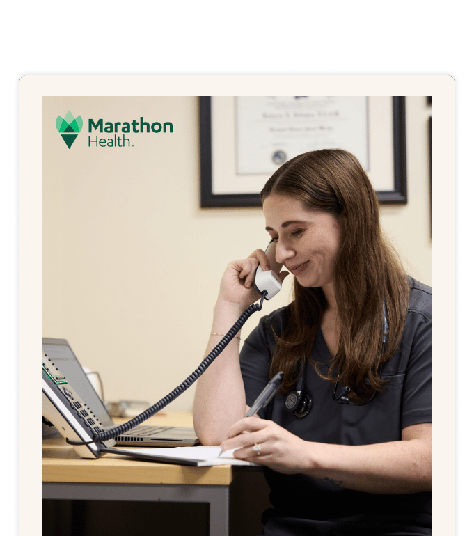 Healthcare provider in scrubs takes notes on a clipboard during a phone call, coordinating a specialty care referral from primary care..