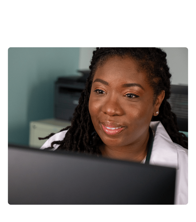 Physician in a white coat working on a computer during a telehealth or advanced primary care session.