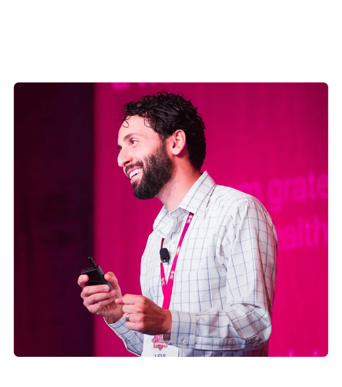 Dr. Levi Rizk speaking on a pink-lit stage at a conference event.