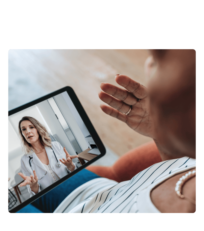 Person gesturing during a virtual care video call with a healthcare provider in a white coat on a tablet screen.