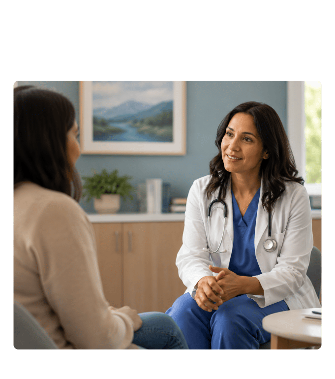 Healthcare provider in a white coat and stethoscope conversing with a person in a clinic office setting
