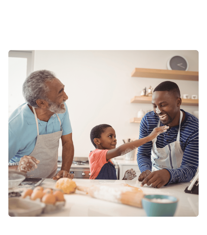 Multigenerational family members laughing together while baking in a kitchen, with flour and eggs on the counter.