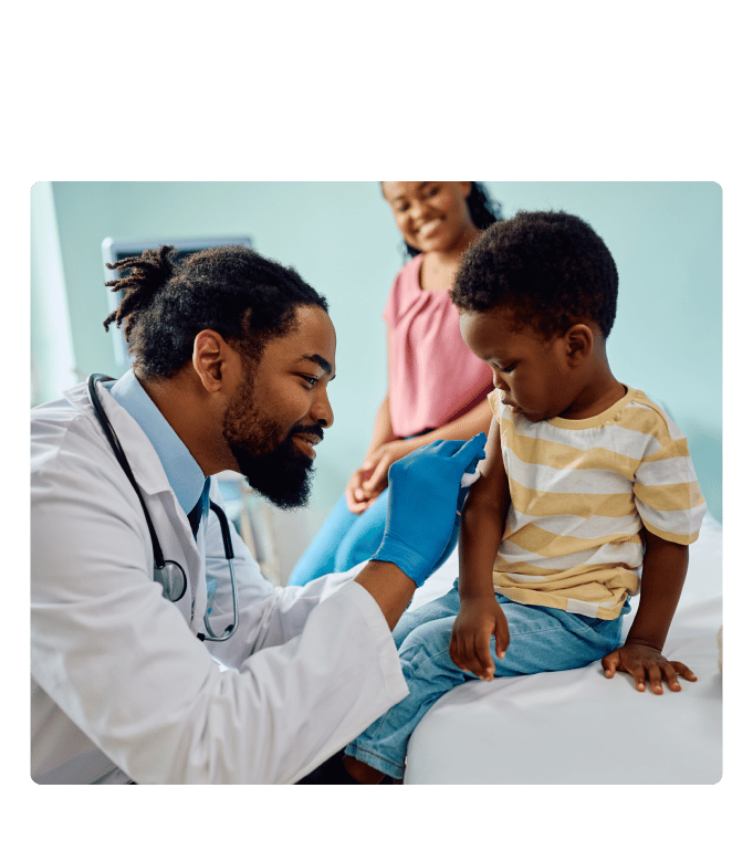Doctor administering a vaccine to a child on an exam table while an adult looks on in a clinic.