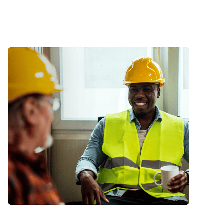 Two union workers in hard hats and safety vests having a conversation in an office setting.
