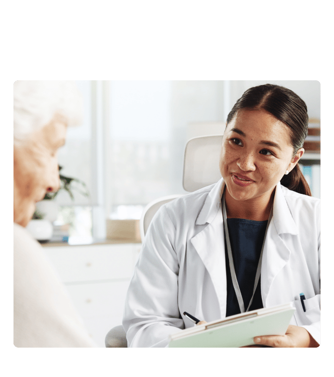 Health coach in a white coat holding a clipboard during a conversation at a primary care clinic.