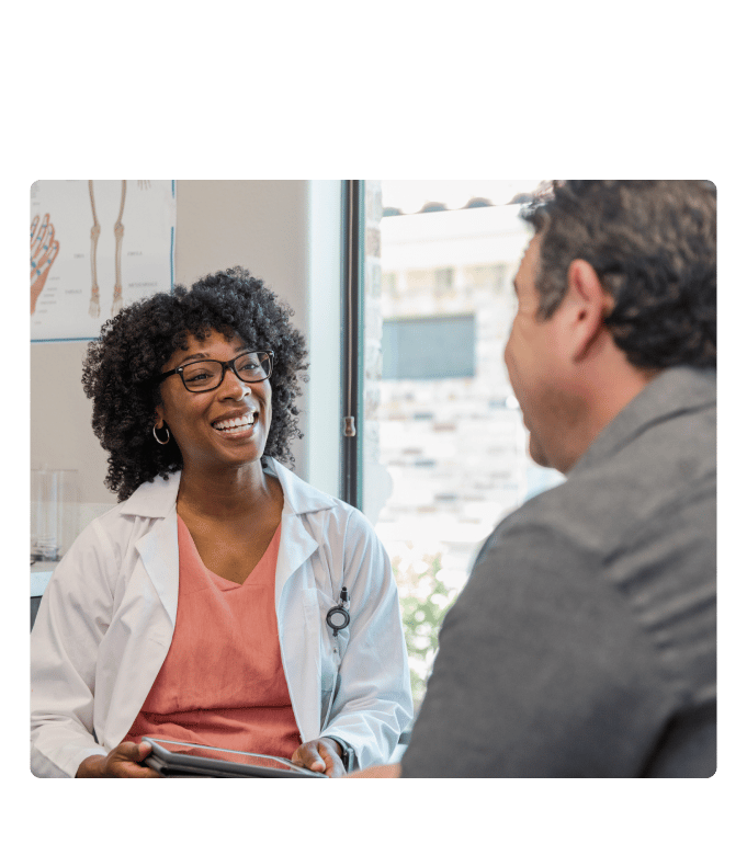 Healthcare provider in a white coat smiling during a conversation with a person at a primary care clinic.