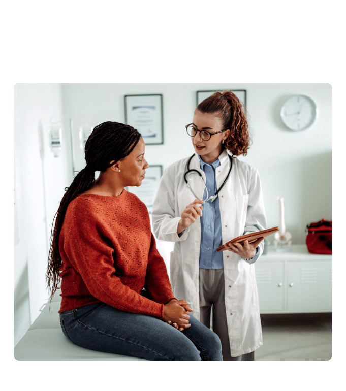 Healthcare provider in a white coat reviewing a clipboard with a person seated in a clinical exam room