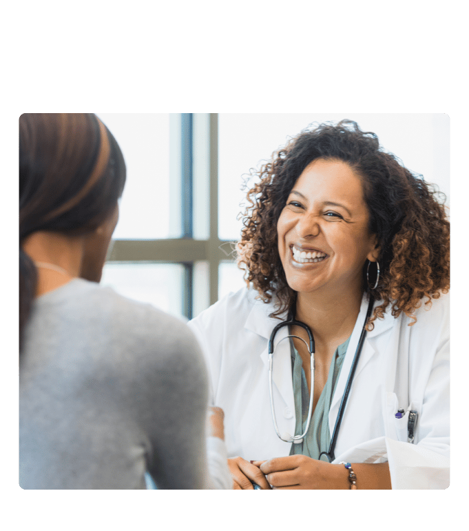 Healthcare provider in a white coat and stethoscope smiling during a conversation at a primary care clinic.