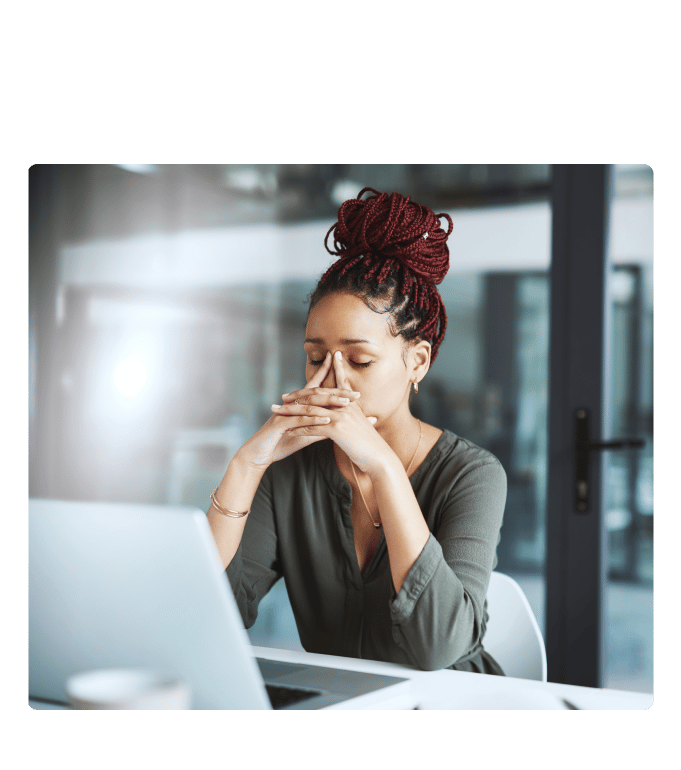 Tired employee sitting at a desk with a laptop, hands raised to face, in an office setting.