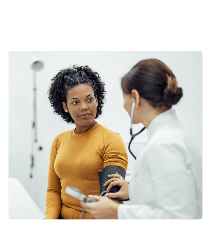 Healthcare provider in a white coat taking a person's blood pressure in a clinical setting.