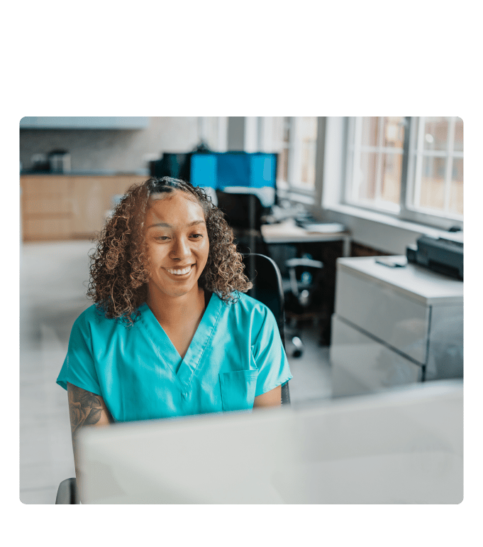 Referral coordinator smiling while working at a computer in a clinic office.