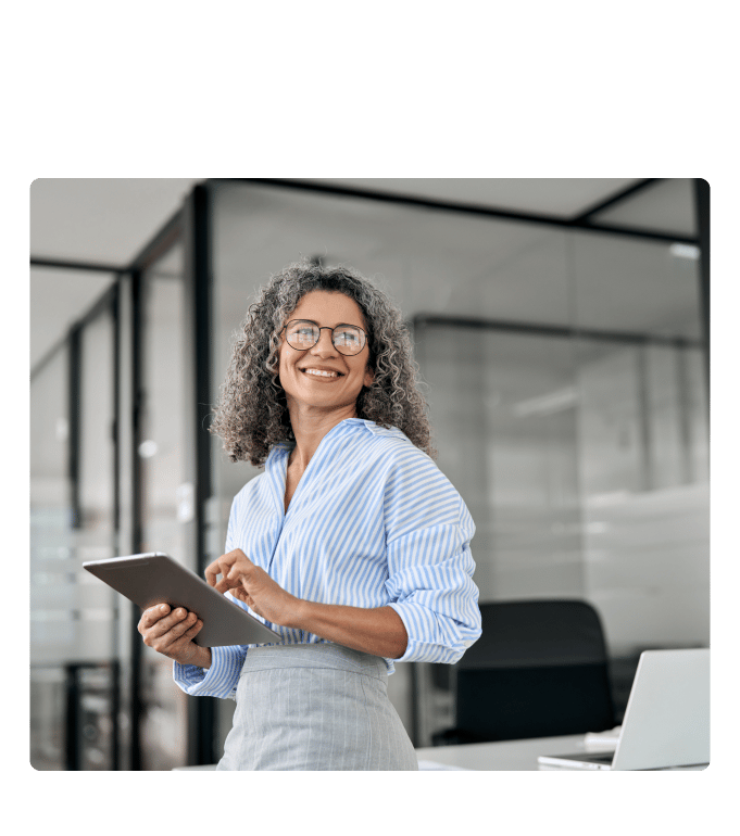 Person wearing glasses holding a tablet and smiling in a modern office setting
