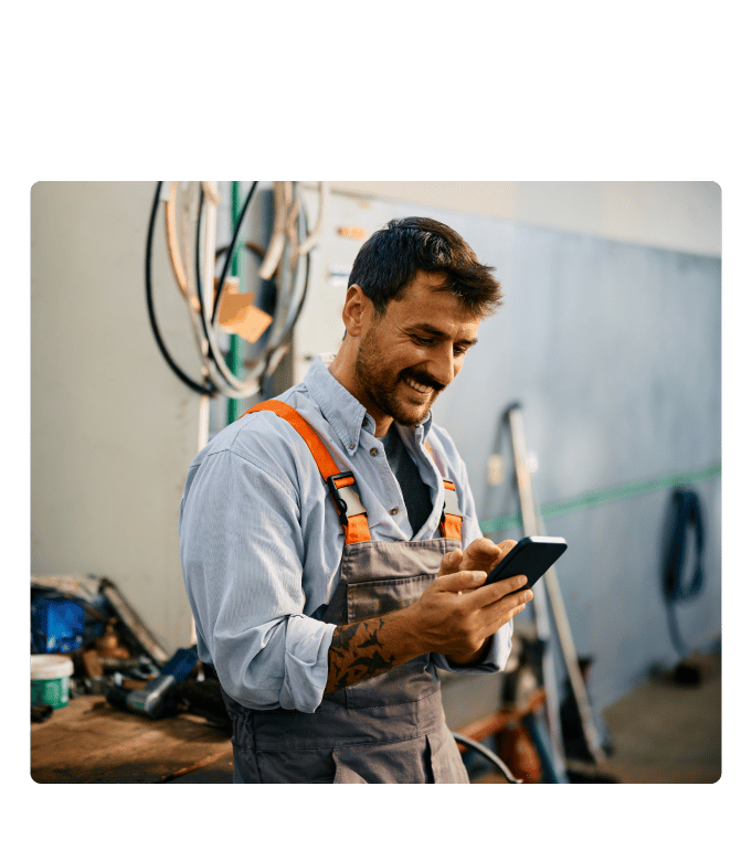 Worker in overalls accessing his employee healthcare benefits via smartphone in an industrial workshop setting.