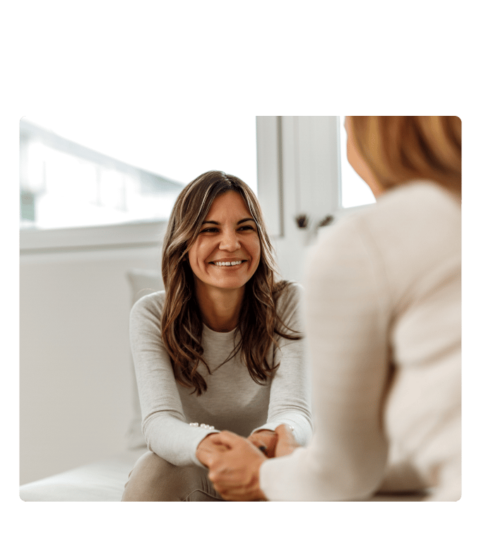 Two people in conversation in a bright office setting, one smiling warmly toward the other