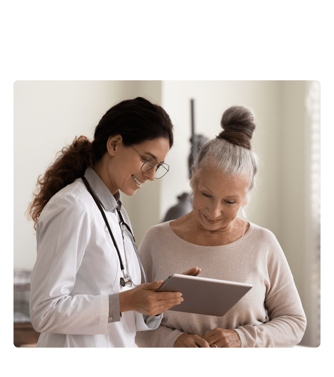 Healthcare provider reviewing a tablet with a person in a bright clinical setting.