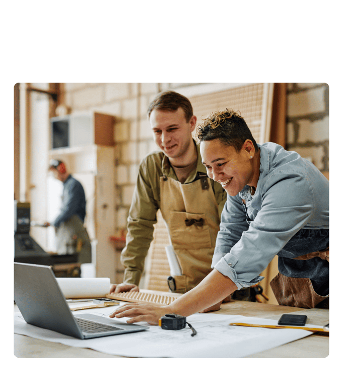 Two workers in aprons conducting an ergonomic assessment on a laptop in an industrial workshop.
