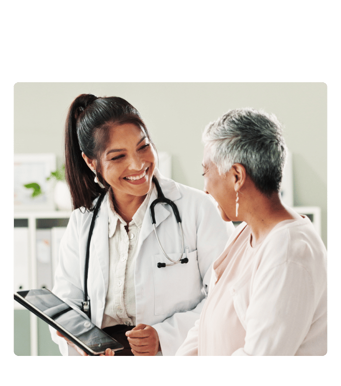 Direct-to-employer healthcare provider in a white coat and stethoscope reviewing a tablet with a person in a clinic setting.