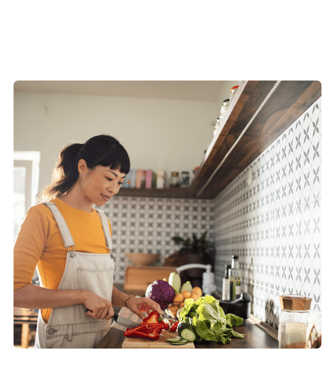 Person chopping fresh red pepper and vegetables on a kitchen counter surrounded by colorful produce