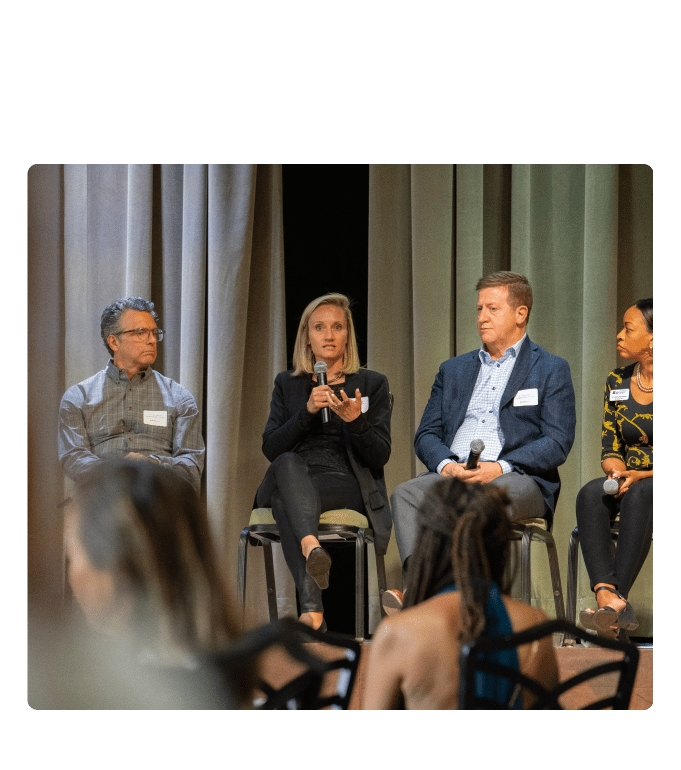Four panelists seated on a stage speak with microphones before an audience
