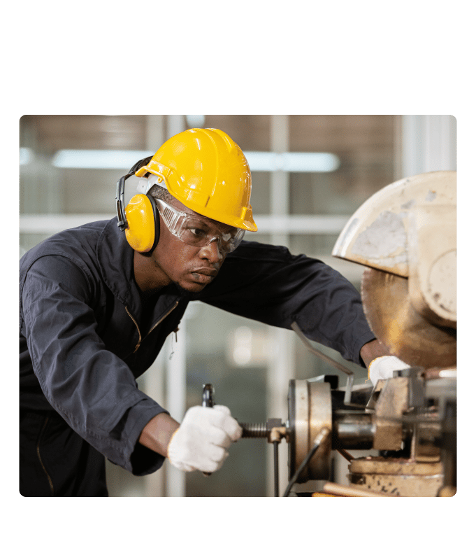 Worker in a yellow hard hat, safety glasses and gloves operates industrial machinery