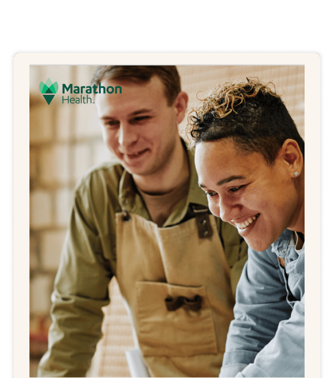 Two smiling workers in aprons looking down together at something out of frame