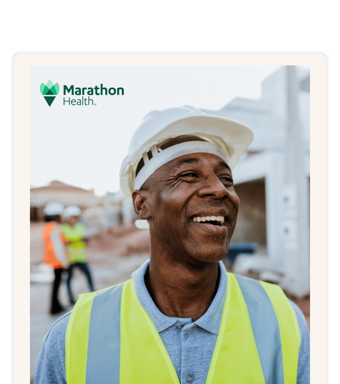 A worker in a hard hat and high-visibility vest smiles at a construction site, with two workers visible in the background