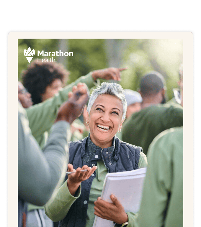 A smiling person holding papers engages with a group of people outdoors