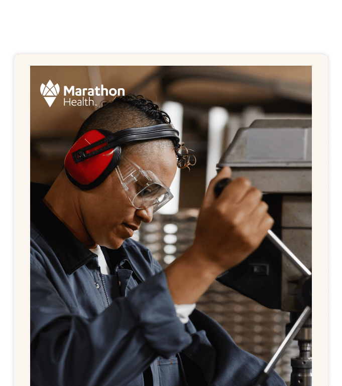 A worker in safety goggles and red ear protection operates industrial equipment in a workshop