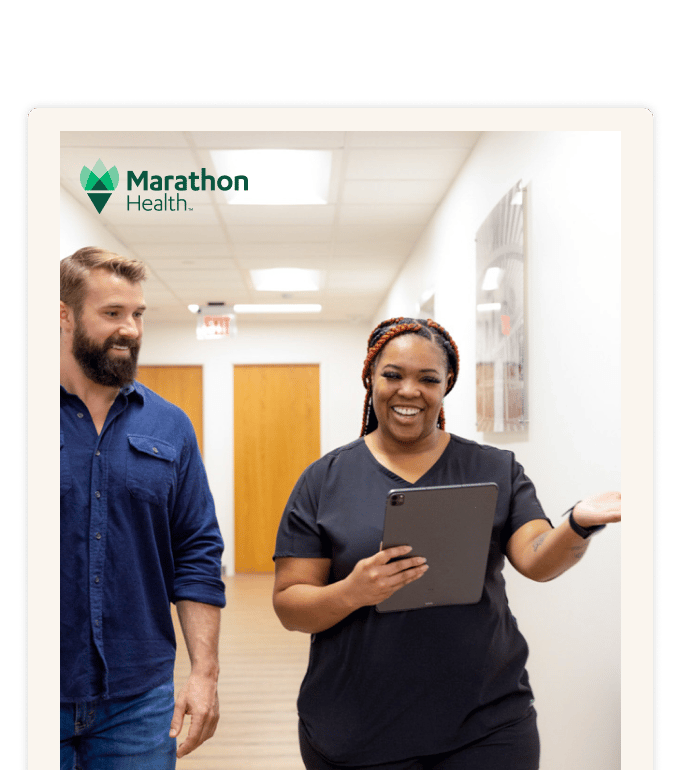 Marathon Health staff member reviewing a tablet with a patient while walking through a health center hallway.