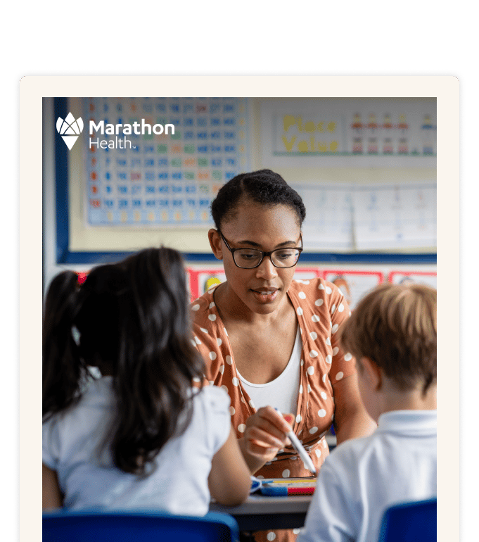 Teacher helps students at a desk in a classroom with educational charts on the wall