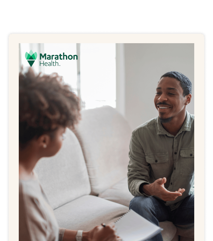 Two people sit across from each other during a LiveBetter mental health session, one smiling and gesturing while the other holds an open notebook.