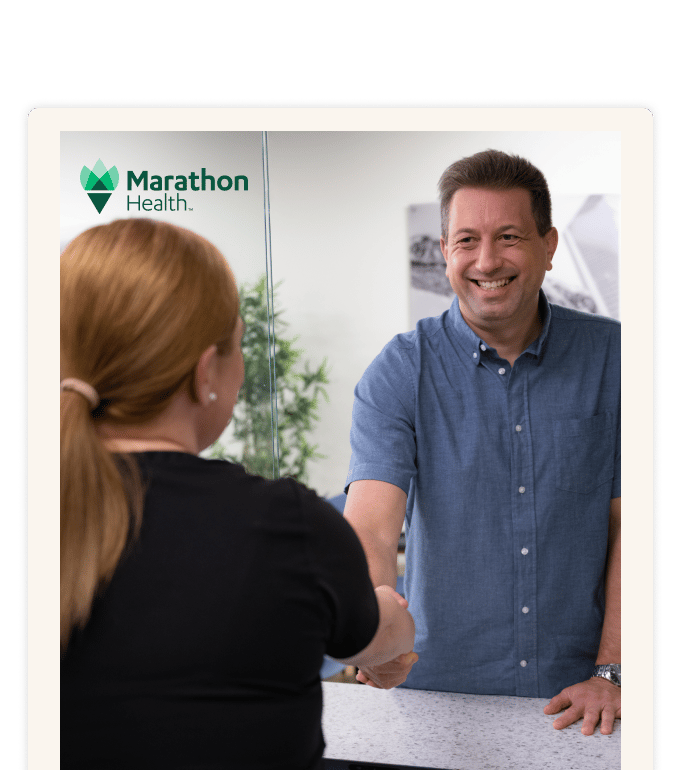 Marathon Health staff member welcoming a patient with a handshake at the front desk.