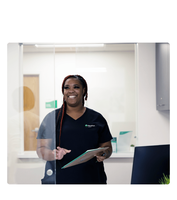 Healthcare professional in scrubs holding a clipboard and smiling inside a Marathon Health clinic