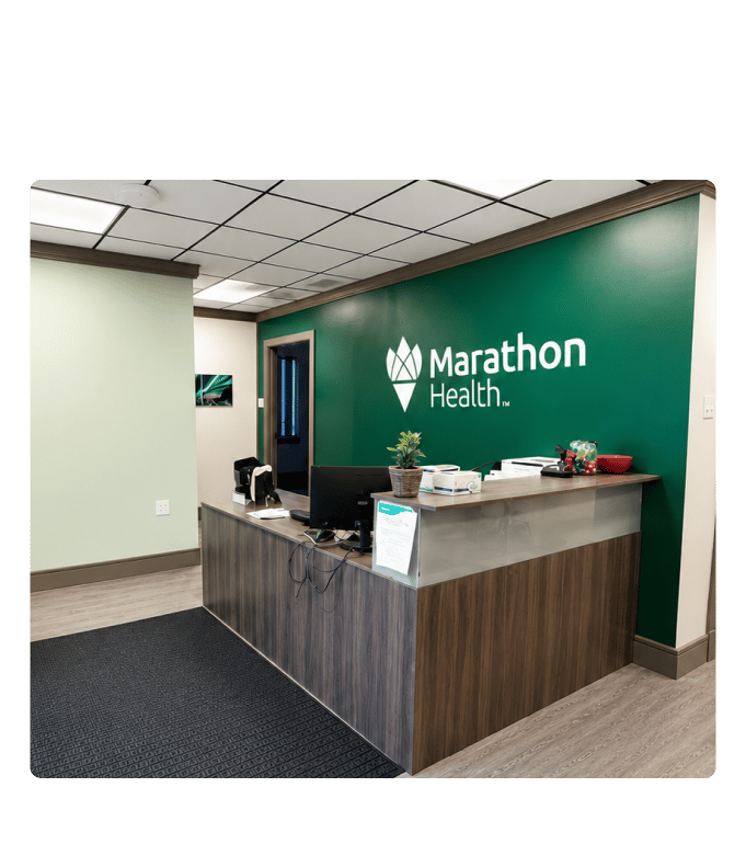 Marathon Health employee health center reception desk with branded green accent wall and logo signage