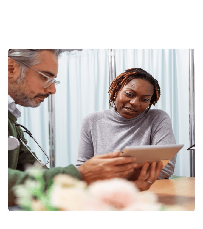Healthcare provider with a stethoscope reviewing a tablet with a person at a primary care clinic