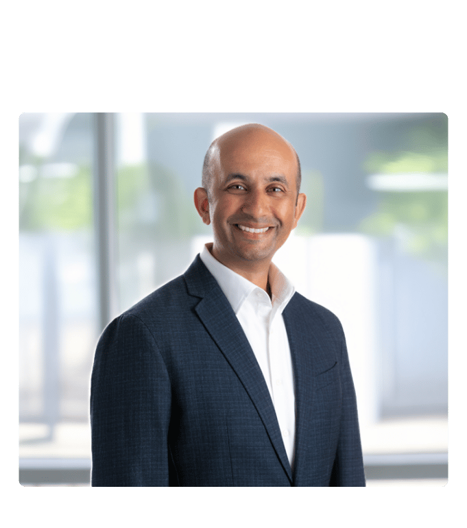 Dr. Nirav Vakharia smiling in a navy blazer and white shirt against a bright office background