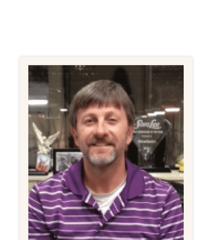 Craig Borden smiling in a purple striped polo shirt, seated in an office with awards and framed photos visible behind him