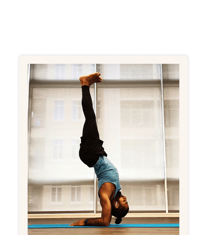 Gurveer Uppal performing a headstand on a blue yoga mat in a bright studio with large windows