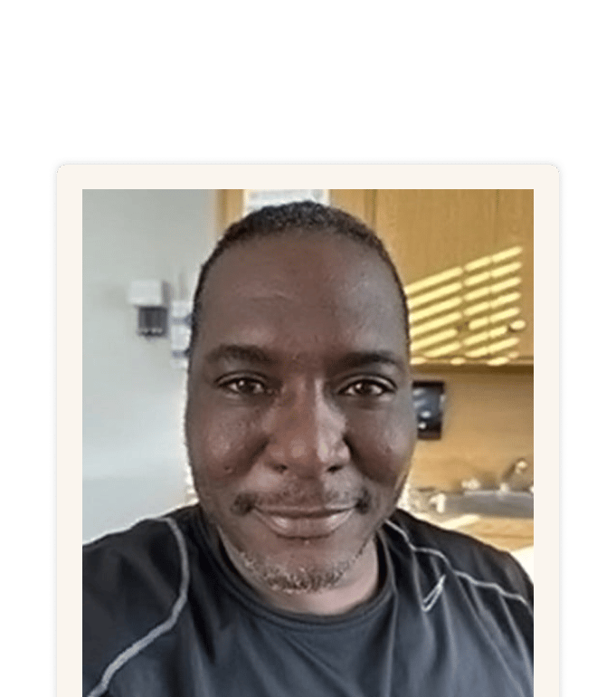 Darryl Blackman smiling in a selfie, wearing a dark athletic shirt, with wood cabinets and a sink visible behind him