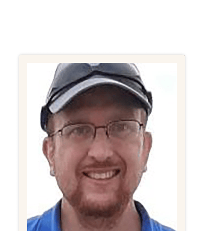 Brian smiling in a close-up portrait, wearing glasses and a dark baseball cap with a blue polo shirt