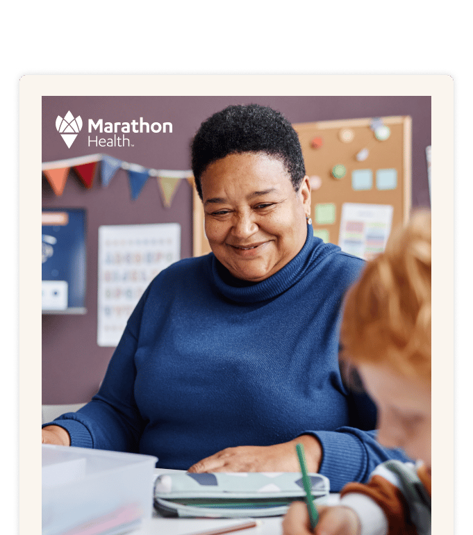 A smiling adult in a blue sweater at a classroom table with a child.