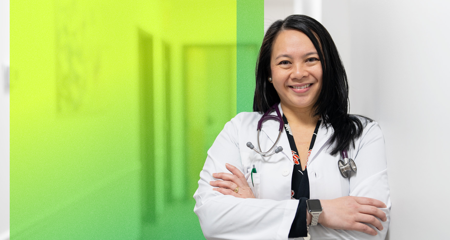Smiling healthcare provider in a white coat and stethoscope stands arms crossed beside the Keller ISD logo