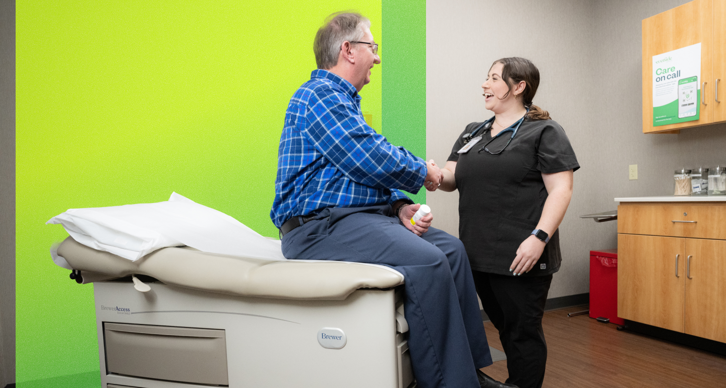 Healthcare provider shakes hands with a smiling person seated on an exam table in a bright green exam room