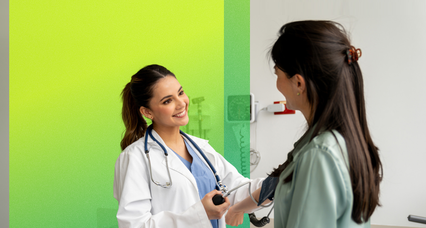 Smiling provider in a white coat takes a person's blood pressure in an exam room with a bright green wall