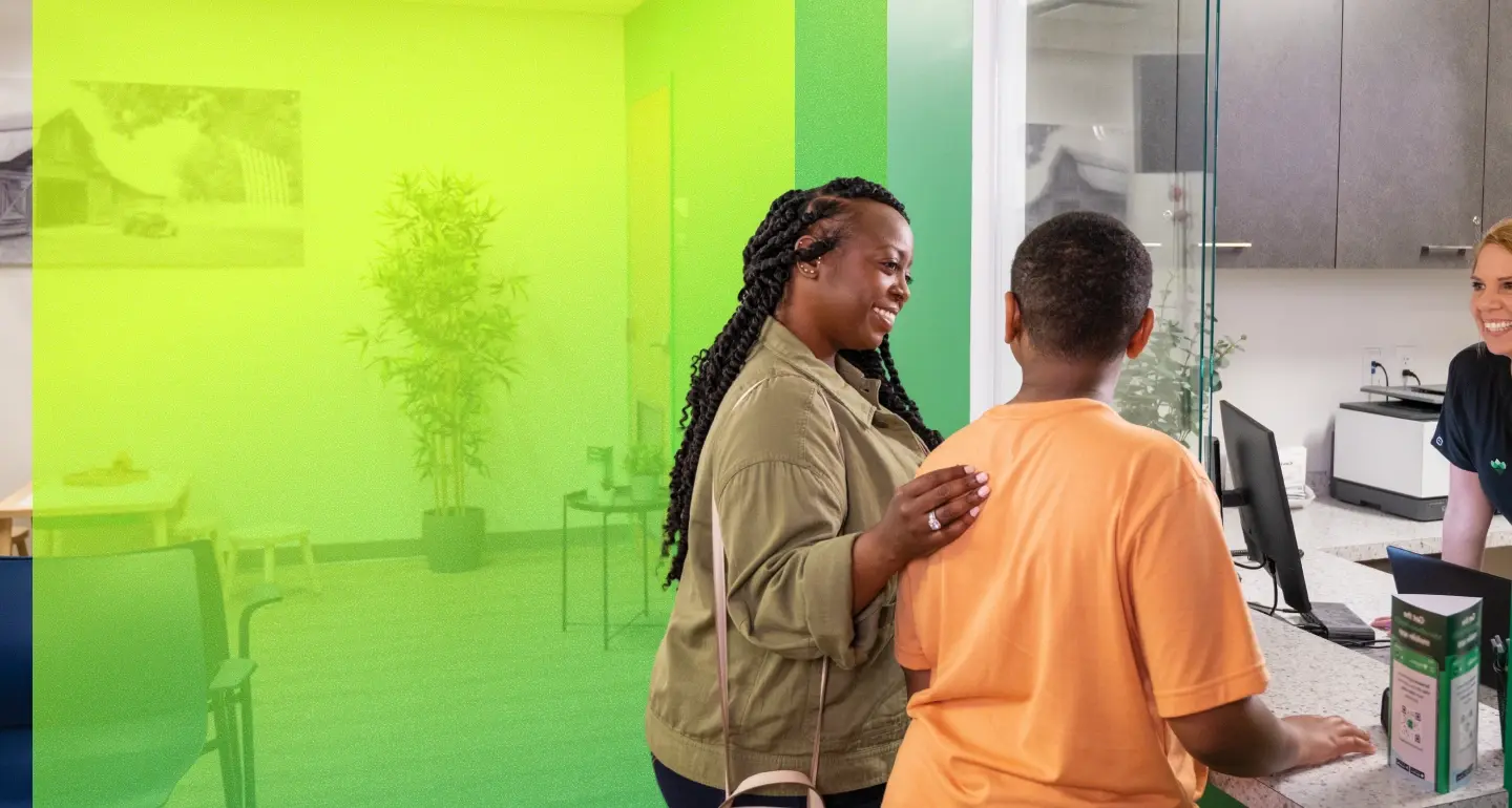 Two people smile at a reception desk inside a Mecklenburg County facility, greeted by a smiling professional.