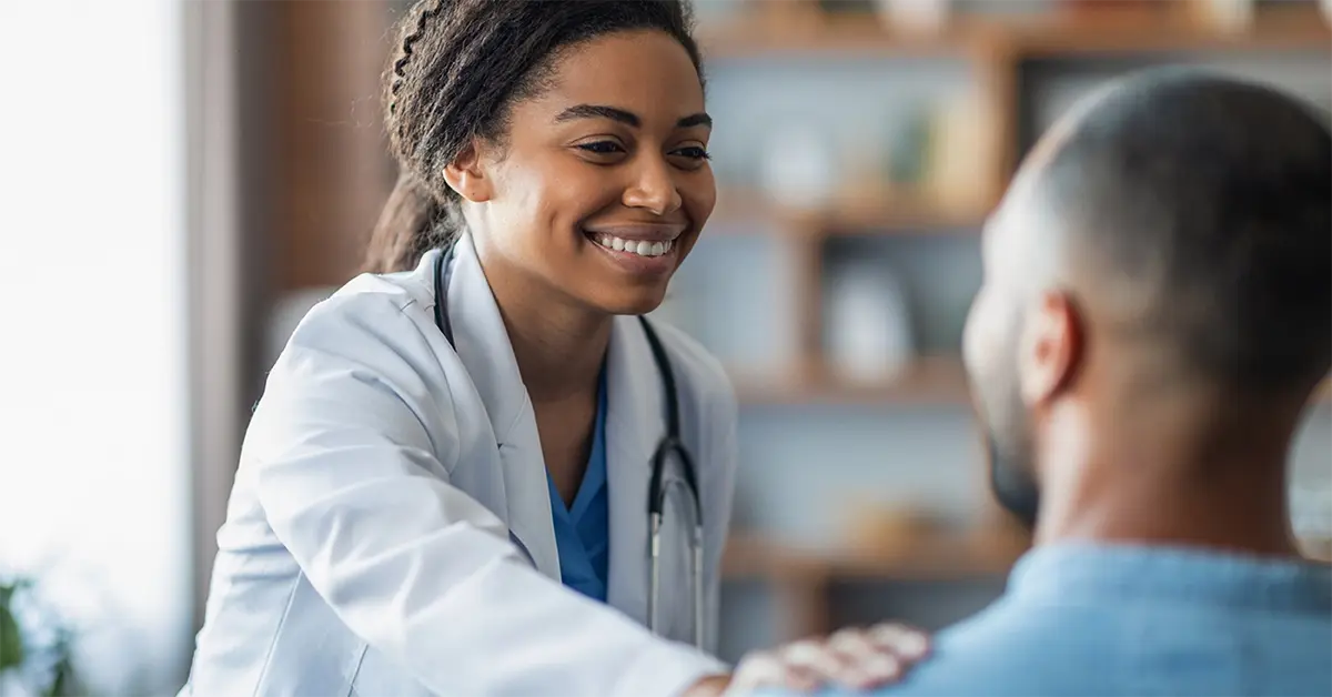 A smiling mental health doctor comforting her patient by putting her hand on his shoulder. 
