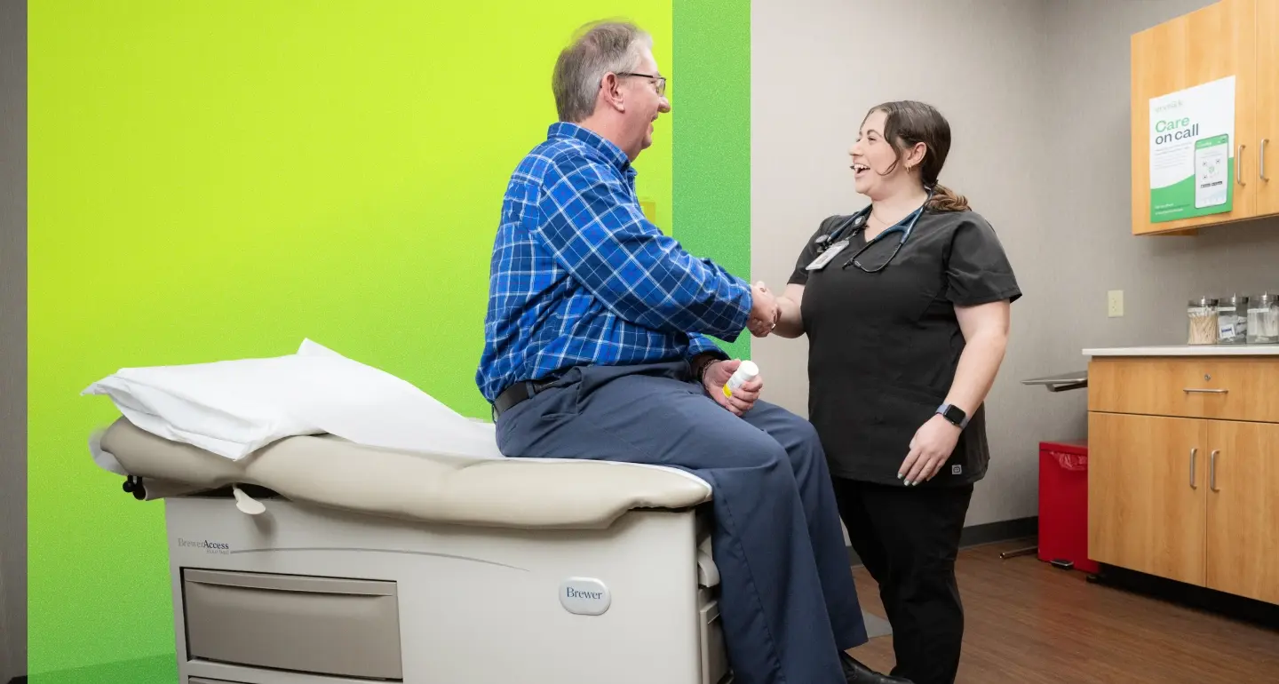 Healthcare provider shakes hands with a smiling person seated on an exam table in a bright green exam room